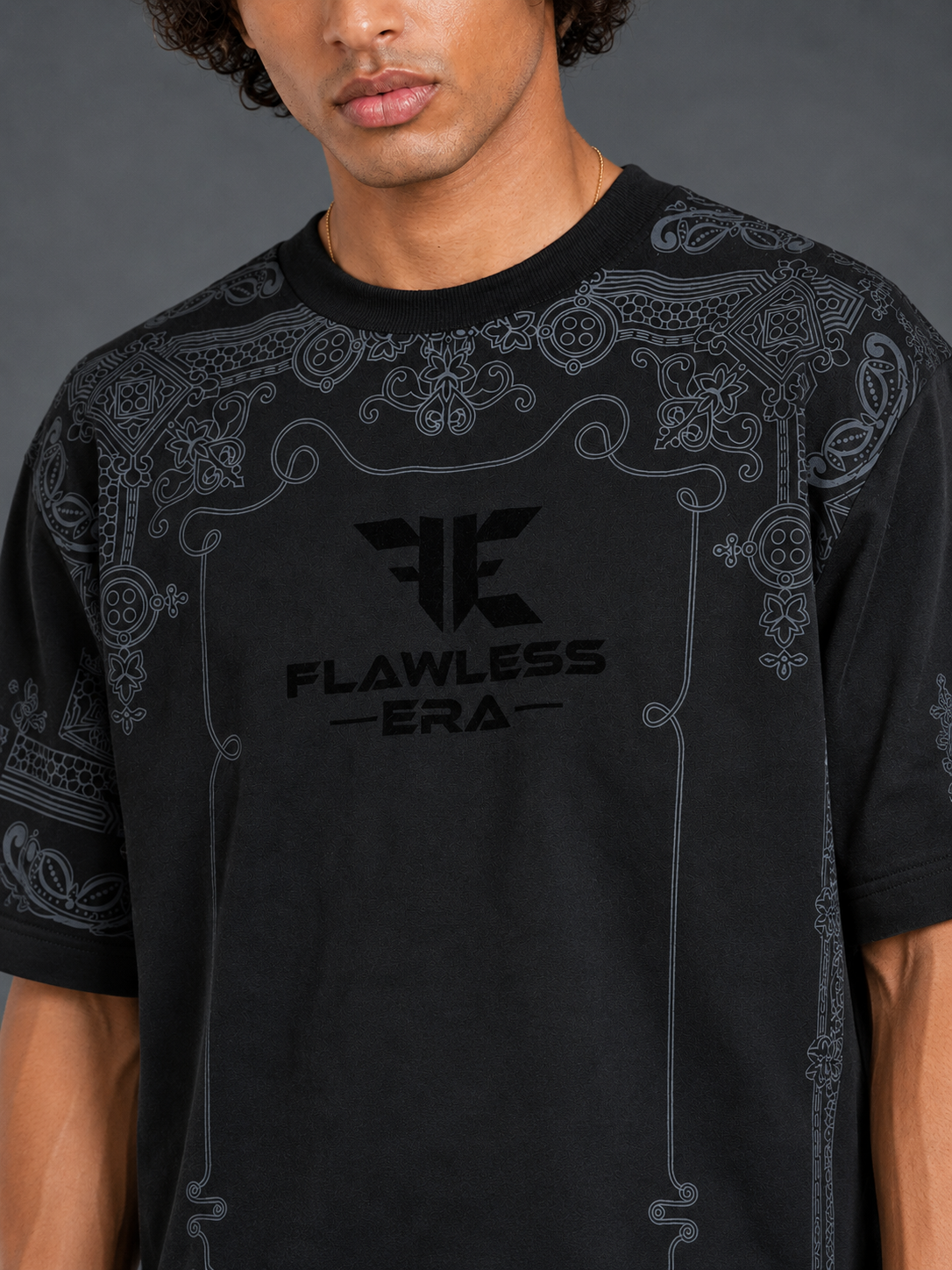 A man wearing a black short-sleeve t-shirt with a dark gray paisley pattern and a black 'Flawless Era' logo printed on the chest.